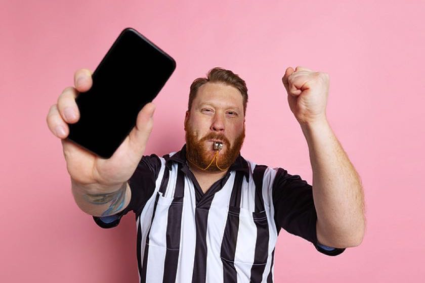 Ref holding his phone and blowing whistle